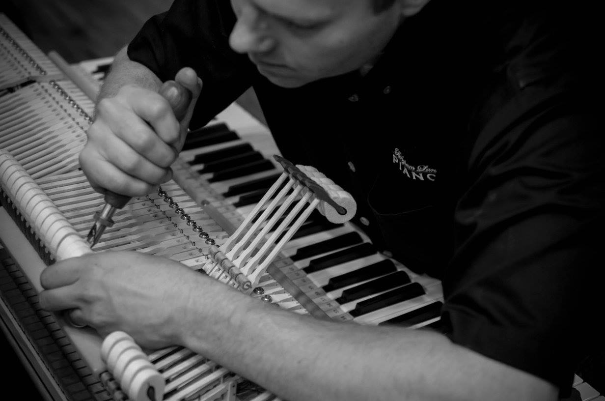 Brigham Larson tuning a grand piano on the Brigham Larson Pianos showroom piano sales floor filled with new and restored grand and upright pianos.