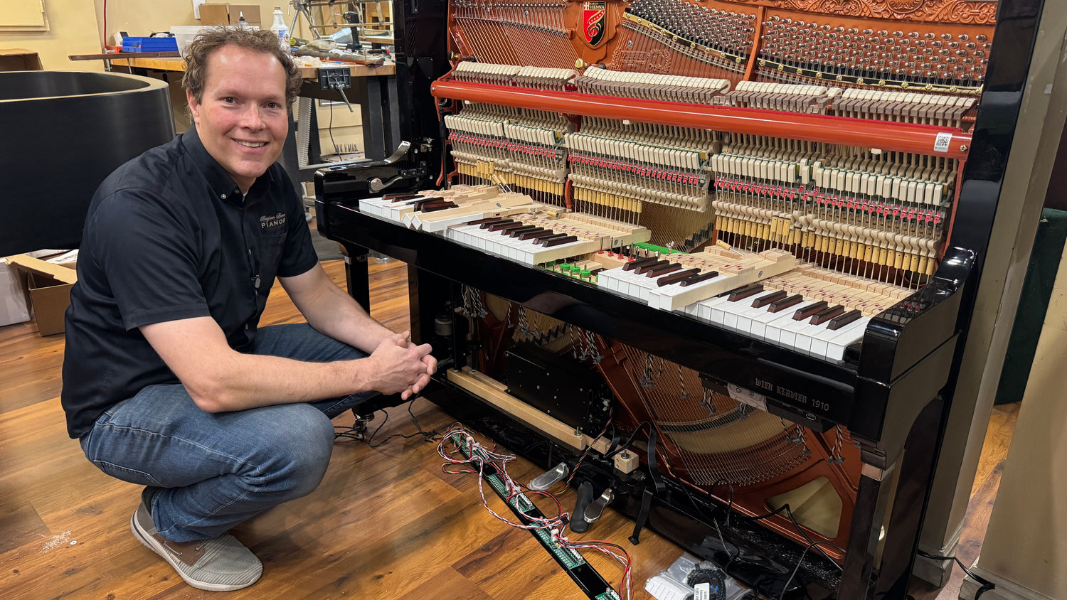 Man kneeling next to an open piano in a room with musical instruments.