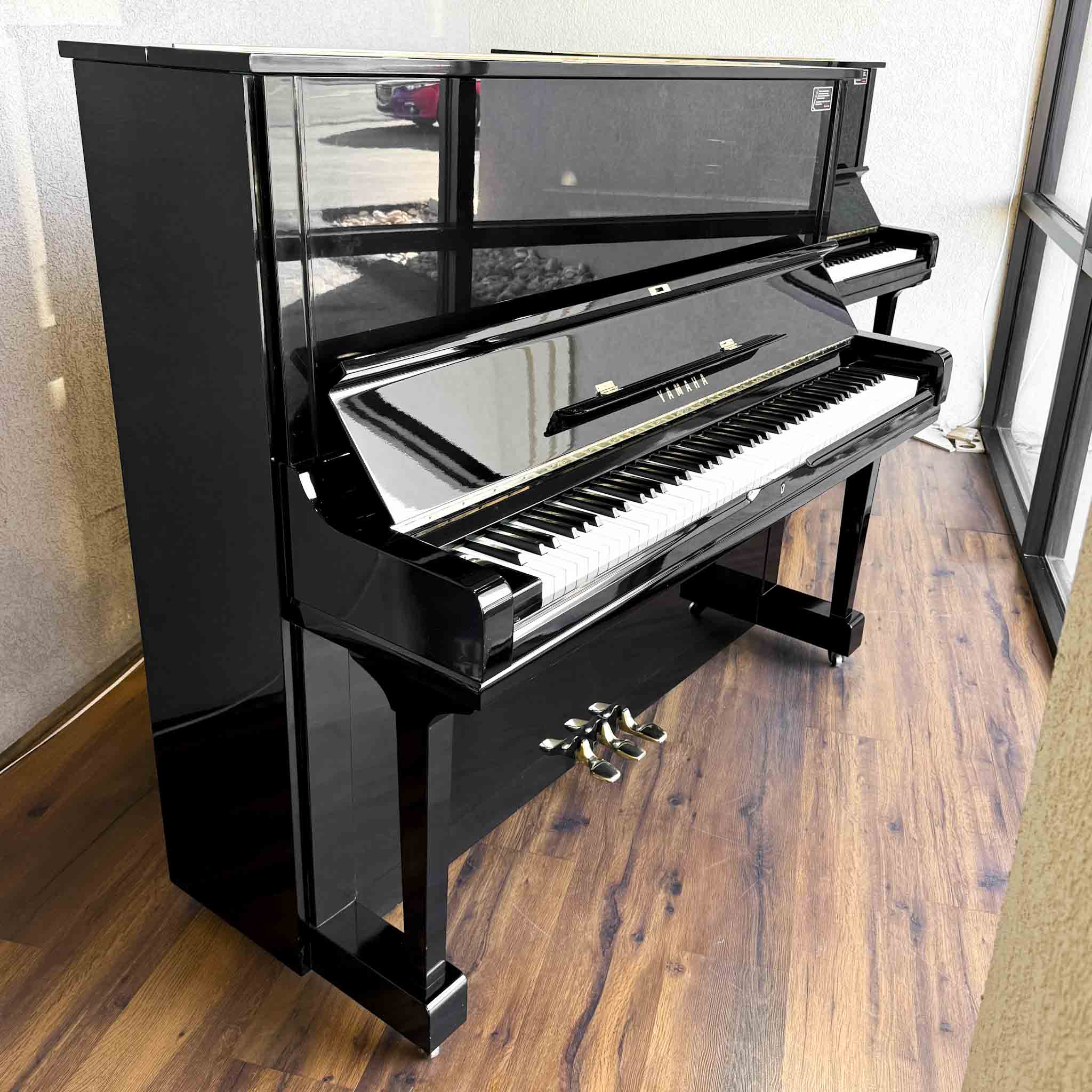 A polished black upright Yamaha U3 piano with a high gloss trim and brass hardware, situated on a wooden floor.