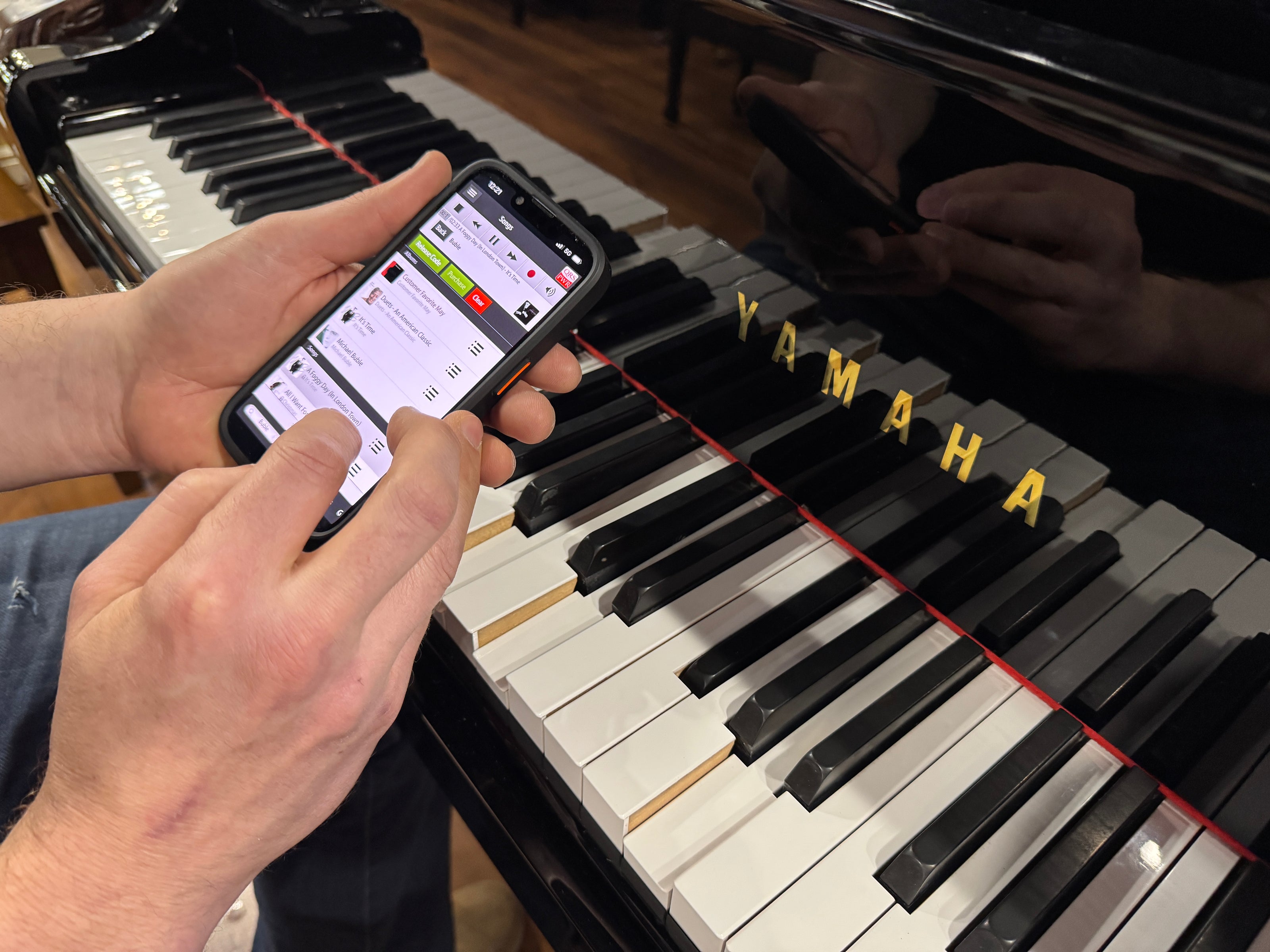 Person using a smartphone QRS piano player app on a Yamaha grand piano keyboard
