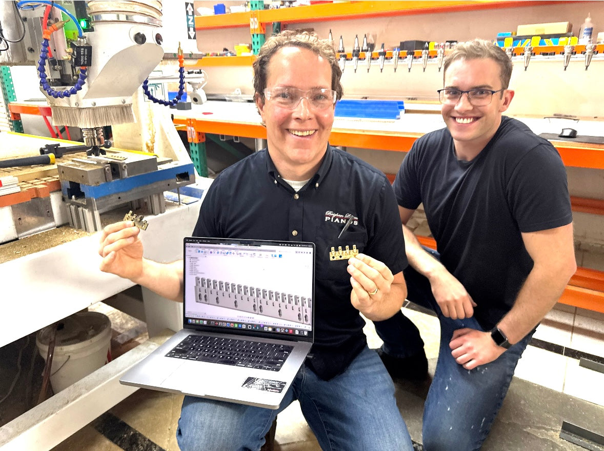 Brigham Larson and Ben Larson kneeling in a workshop with a laptop displaying a software interface showcasing CNC machine technology for restoring brass rails at the Brigham Larson Pianos family heirloom piano restoration shop in Orem, UT.