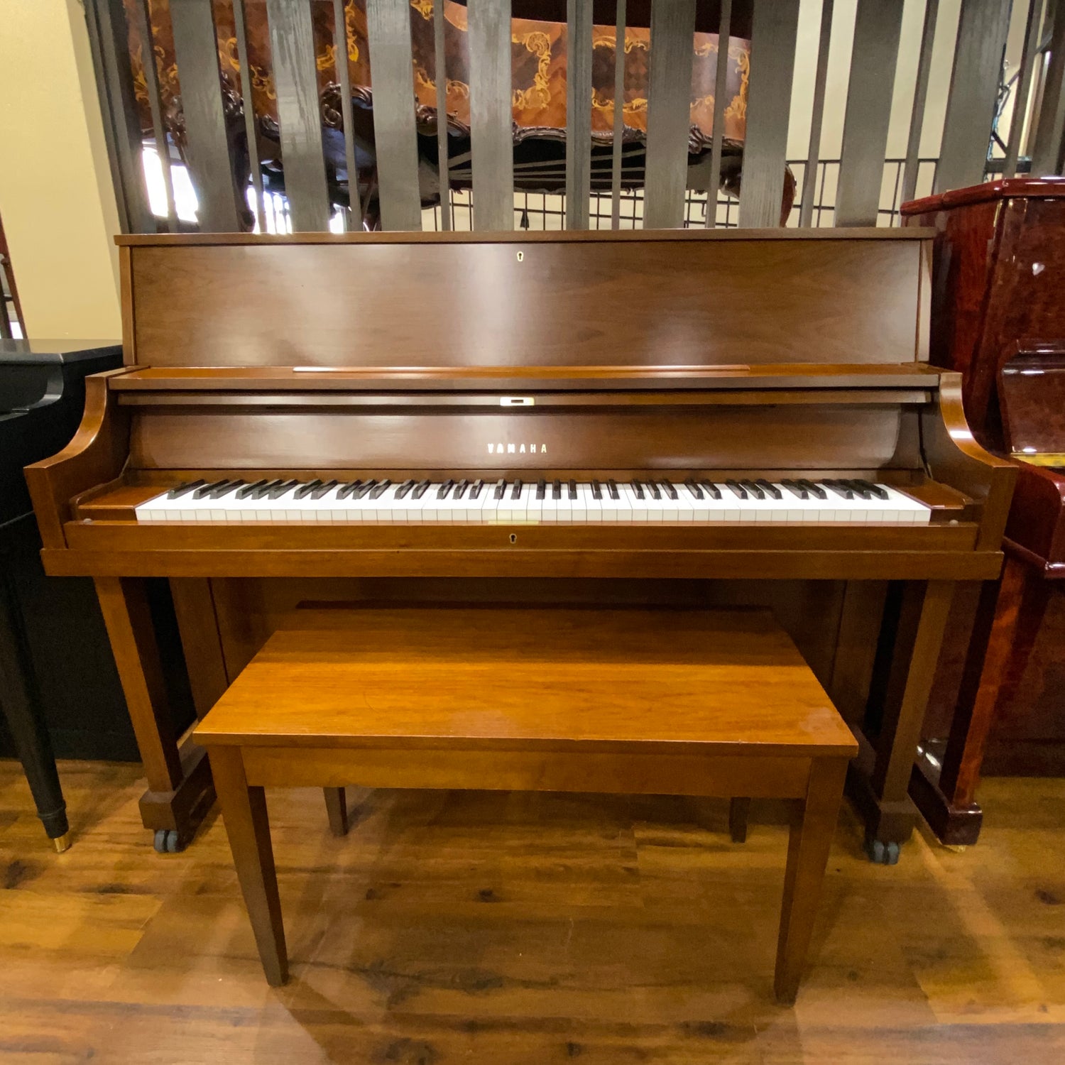 Wooden Yamaha P series upright piano with bench on a wooden piano sales showroom floor