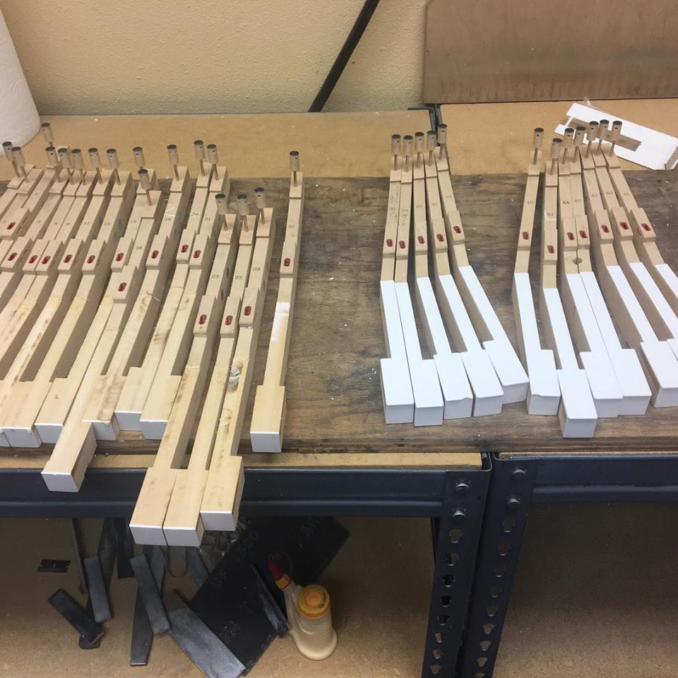 ndividual wooden piano keys with freshly installed white keytops laid out in rows across a workshop table during a keytop restoration process at Brigham Larson Pianos family heirloom piano restoration shop in Orem, UT.