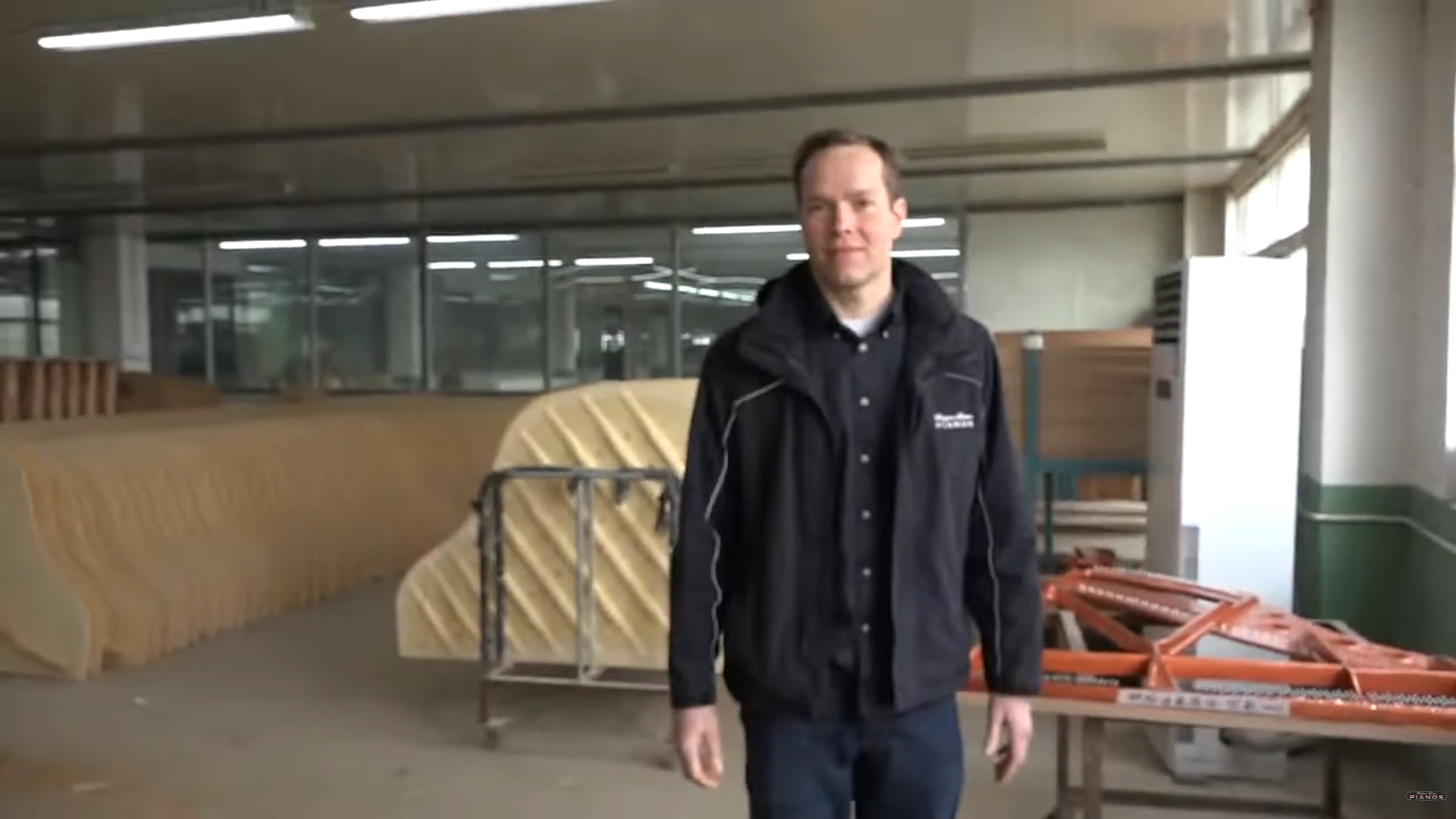 Brigham Larson standing in the Hailun piano factory area with large, unfinished Hailun piano soundboards aligned in a row behind him, located in China.
