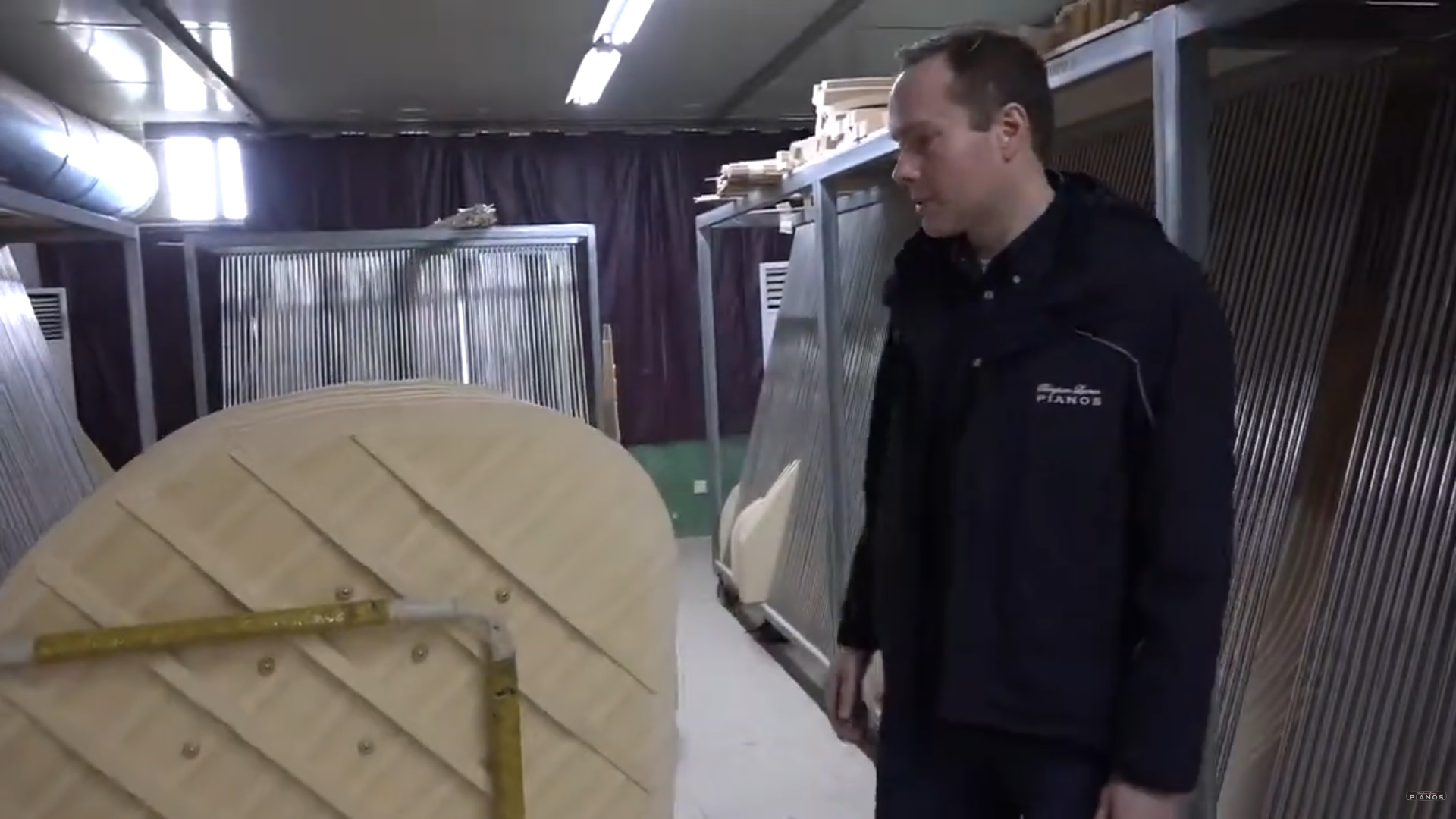 Brigham Larson standing next to a large wooden piano soundboard in the Hailun piano factory in China.
