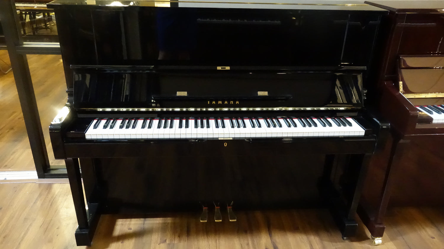 Black Yamaha YUS upright piano on a wooden showroom piano sales floor